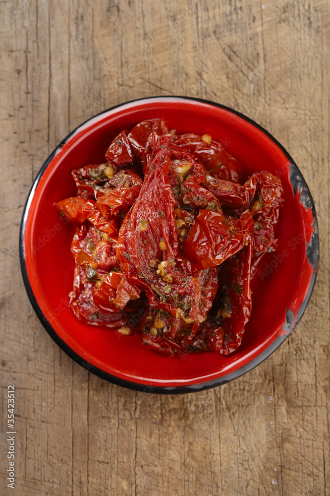 sun-dried tomatoes with olive oil in red enamel dish, old wooden sun-dried tomatoes with olive oil in red enamel dish, old wooden