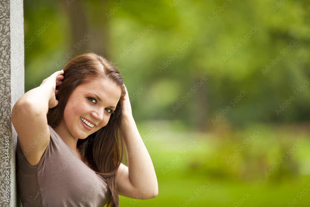 lächelnde hübsche junge Frau im Park lehnt an Säule