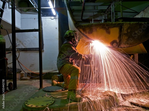 A workman flame cutting a lage metal tank