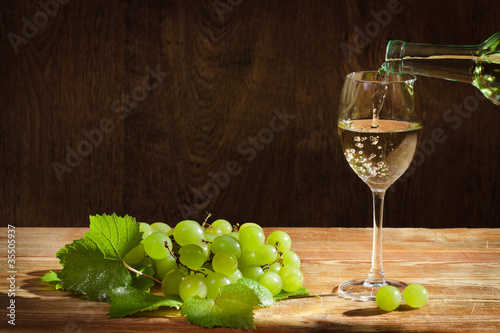 White wine pouring down to the glass with grapes