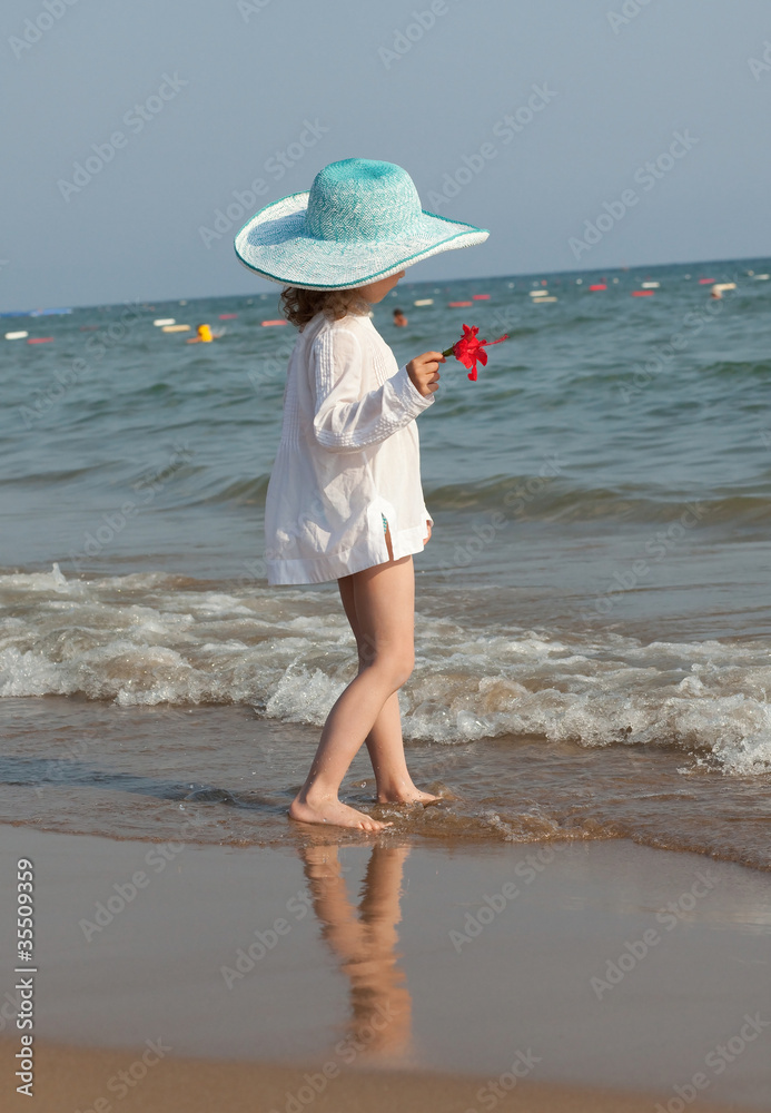 Little girl in the hat looks at the sea.