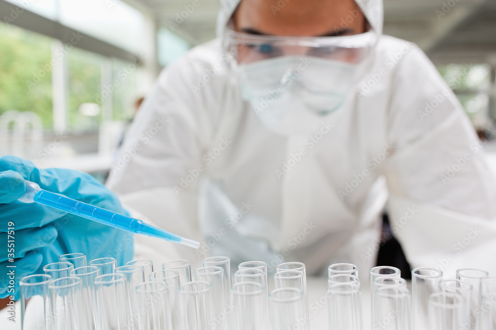 Protected scientist dropping a blue liquid in a test tube Protected scientist dropping a blue liquid in a test tube