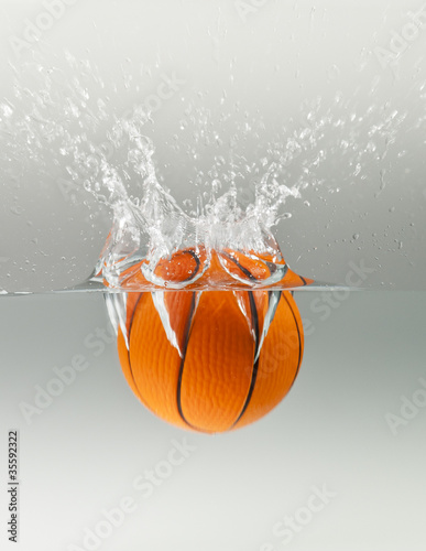 Falling basketball into water isolated on grey background