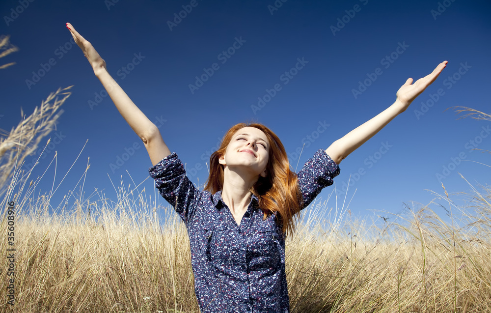 Portrait of happy red-haired girl on autumn grass.