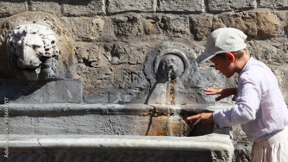 Boy stands and drinks water from old source on wall Boy stands and drinks water from old source on wall
