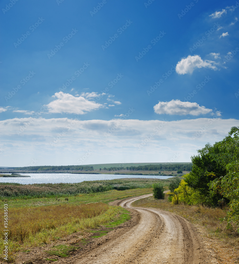 rural road near river under cloudy sky rural road near river under cloudy sky