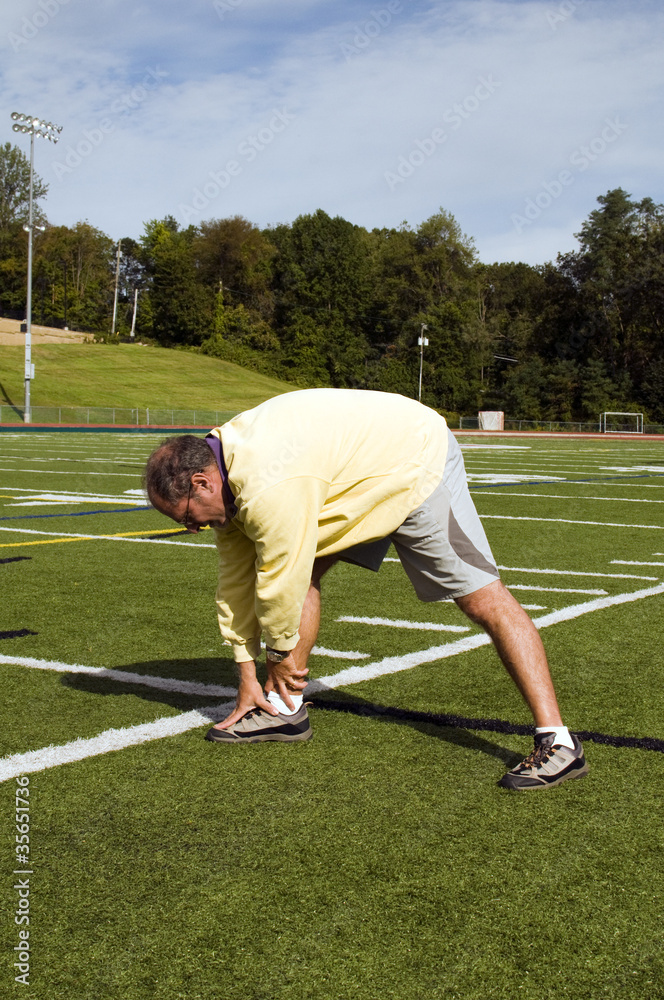 middle age senior man stretching exercising on sports field