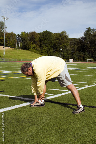 middle age senior man stretching exercising on sports field
