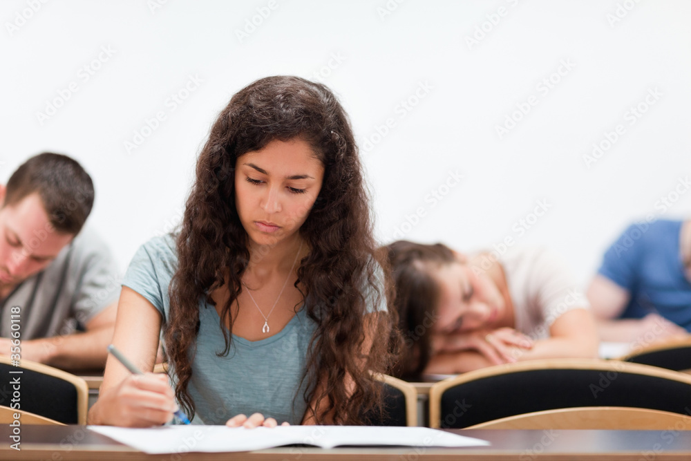 Students writing while their classmate is sleeping Students writing while their classmate is sleeping