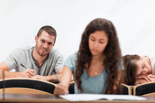 Smiling students writing while their classmate is sleeping