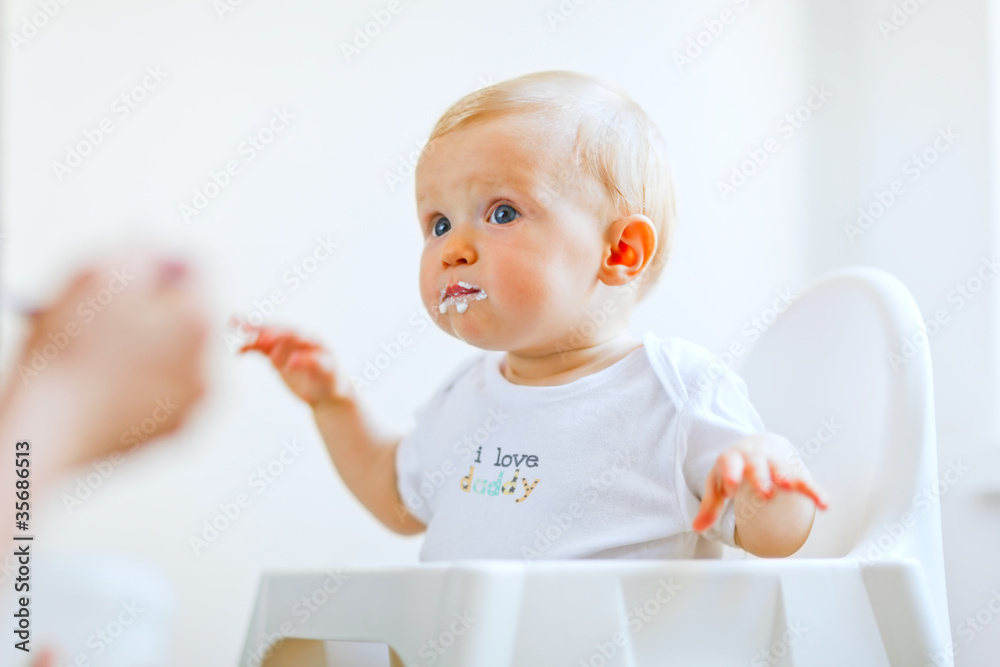 Eat smeared lovely baby in baby chair feeding by mother Eat smeared lovely baby in baby chair feeding by mother