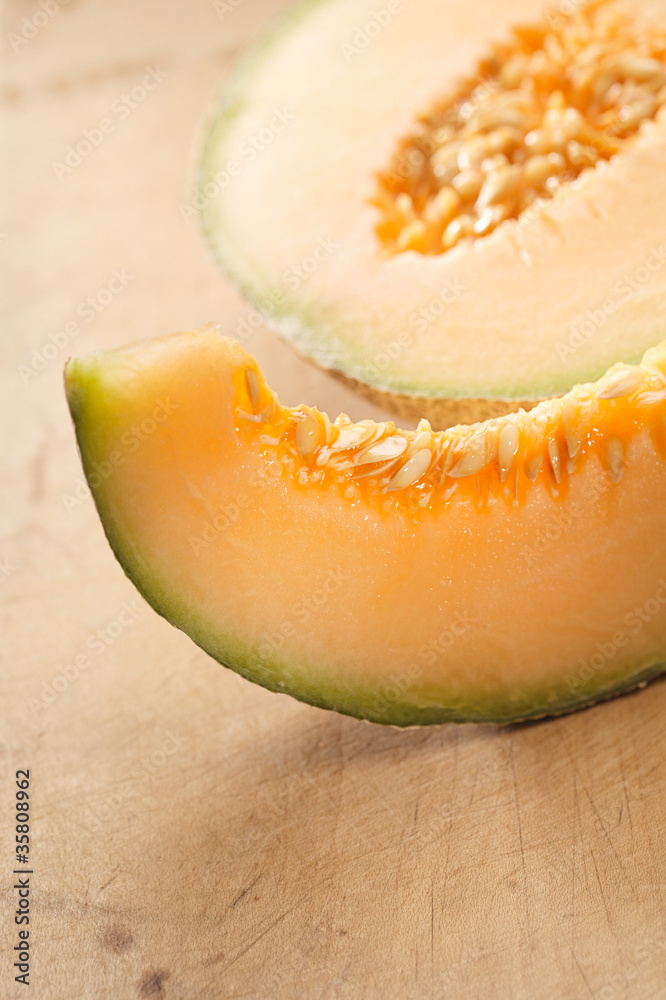 Cantaloupe melon slice and one half on wooden table Cantaloupe melon slice and one half on wooden table