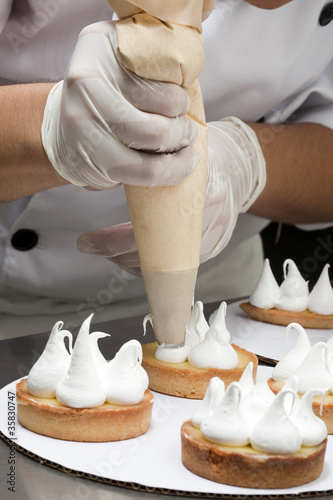 Fototapeta Naklejka Na Ścianę i Meble -  Cuisinier décorant des tartelettes de meringue avec une poche à douille