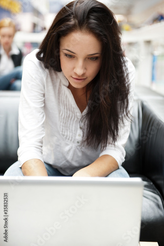 Portrait of a beautiful young woman working on laptop while sitt