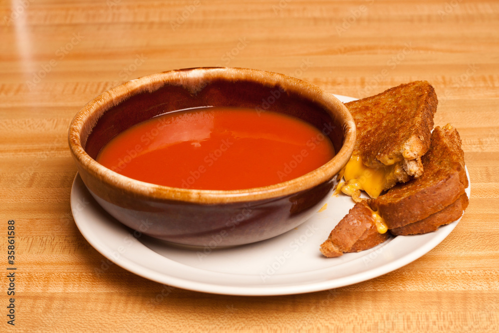 Tomato soup sharing a plate with a cut grilled cheese sandwich Tomato soup sharing a plate with a cut grilled cheese sandwich