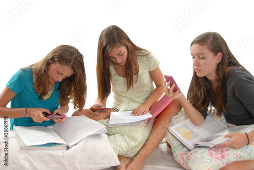Three teenage girls doing homework books phones