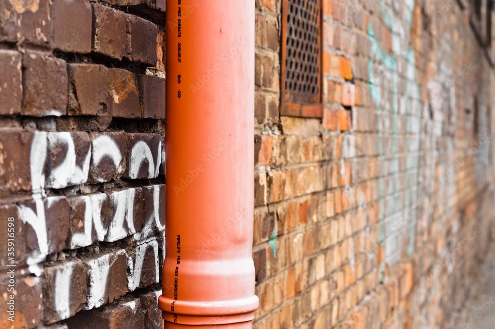 Naklejka premium Sewage pipe on brick abandoned wall