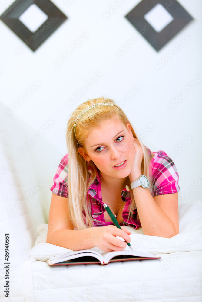 Pensive young woman lying on sofa with notebook and pen Pensive young woman lying on sofa with notebook and pen