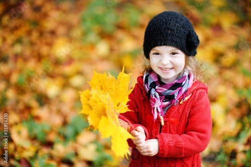 Little girl in a red coat at autumn holding leaves