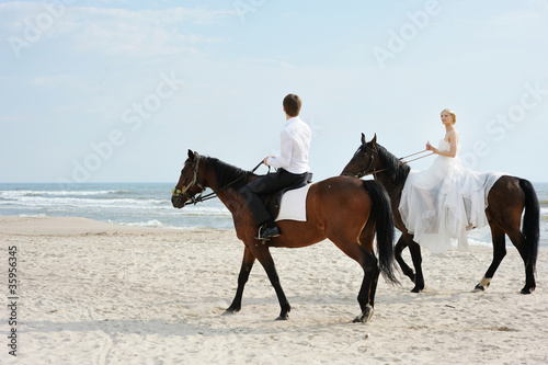 Beach wedding: bride and groom on a horses by the sea