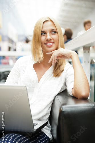 Portrait of happy blond woman using laptop at shopping mall cafe