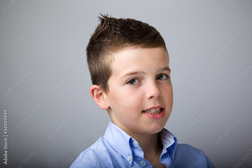 Photo of adorable young boy looking at camera against grey backg Photo of adorable young boy looking at camera against grey backg