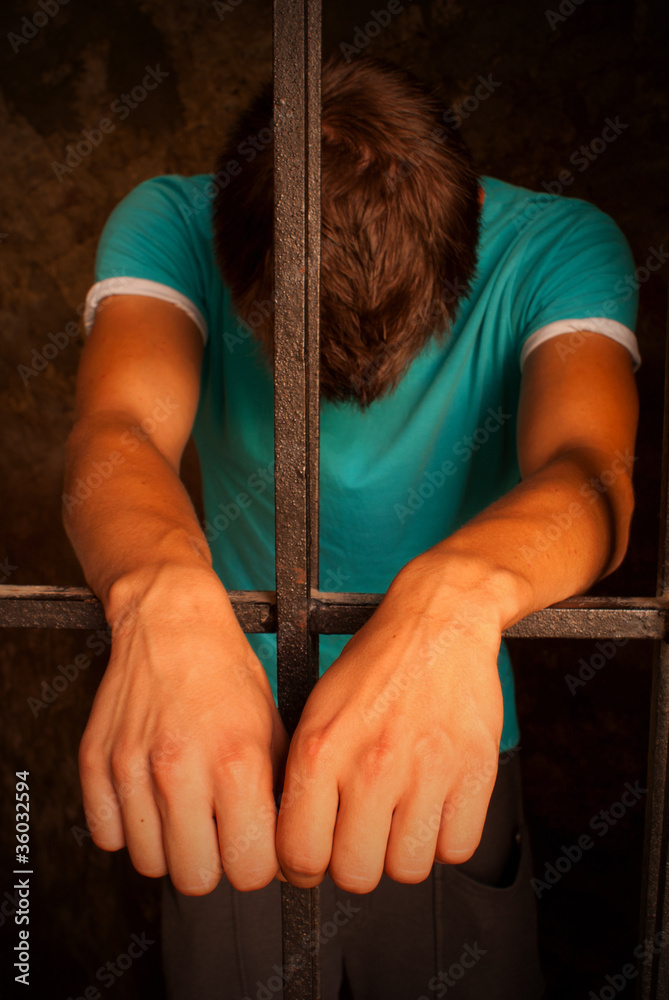 Man with hands tied with rope behind the bars