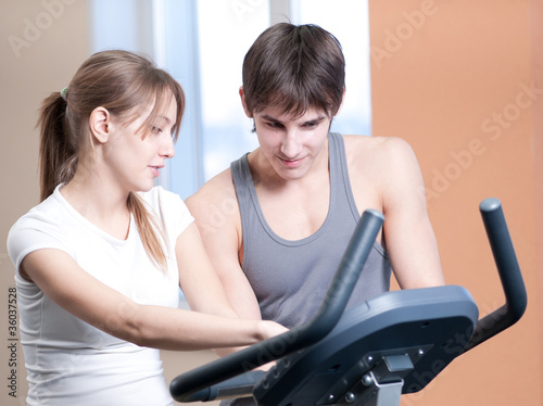 Train on machine in a gym assisted by personal instructor