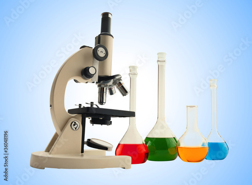 Laboratory metal microscope and test tubes with liquid over blue