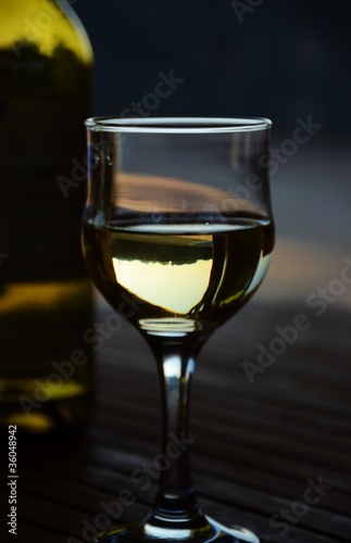Weinglas mit Weisswein und Flasche am Abend