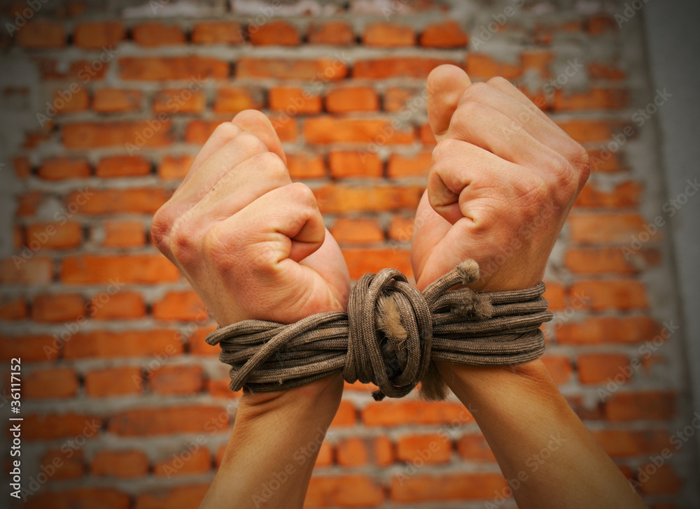Hands tied up with rope against brick wall
