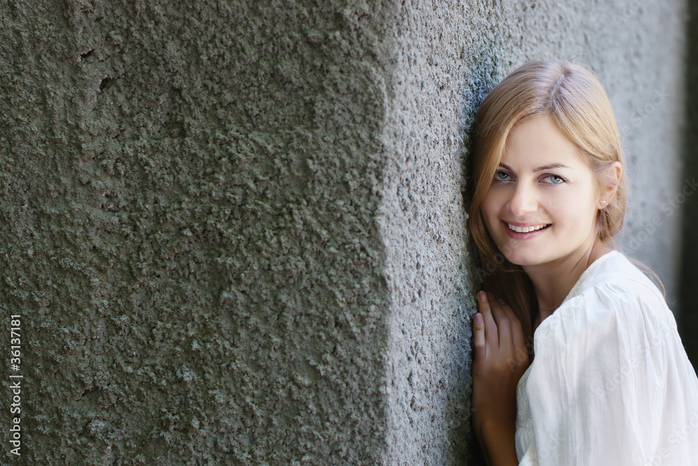 Beautiful blue-eyed smiling woman against rough wall Beautiful blue-eyed smiling woman against rough wall