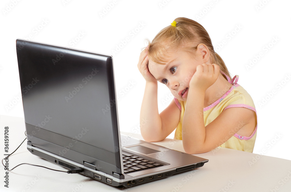 The little girl looks at a computer screen and smiles The little girl looks at a computer screen and smiles