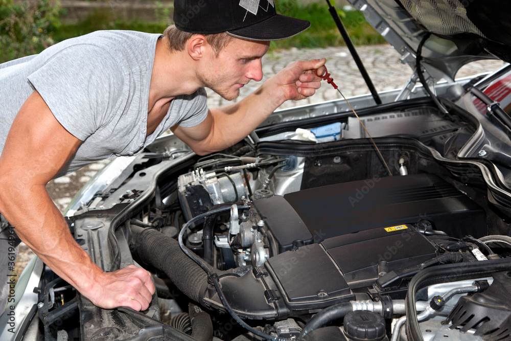 Junger Mann blickt unter die Motorhaube vom PKW Junger Mann blickt unter die Motorhaube vom PKW