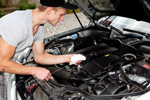 Junger Mann blickt unter die Motorhaube vom PKW