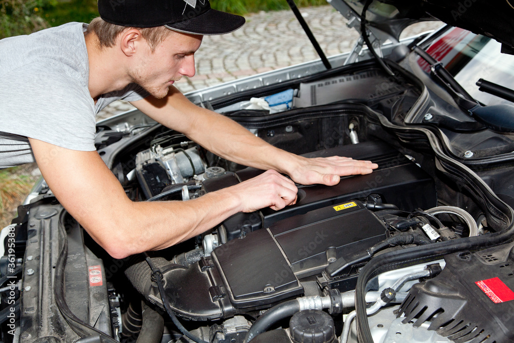 Junger Mann blickt unter die Motorhaube vom PKW Junger Mann blickt unter die Motorhaube vom PKW