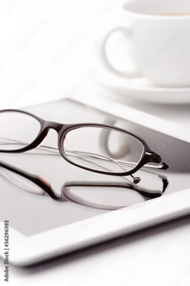 White tablet, coffee cup and glasses on a white table White tablet, coffee cup and glasses on a white table