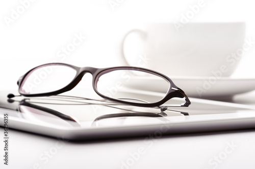 White tablet, coffee cup and glasses on a white table