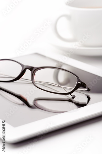 White tablet, coffee cup and glasses on a white table