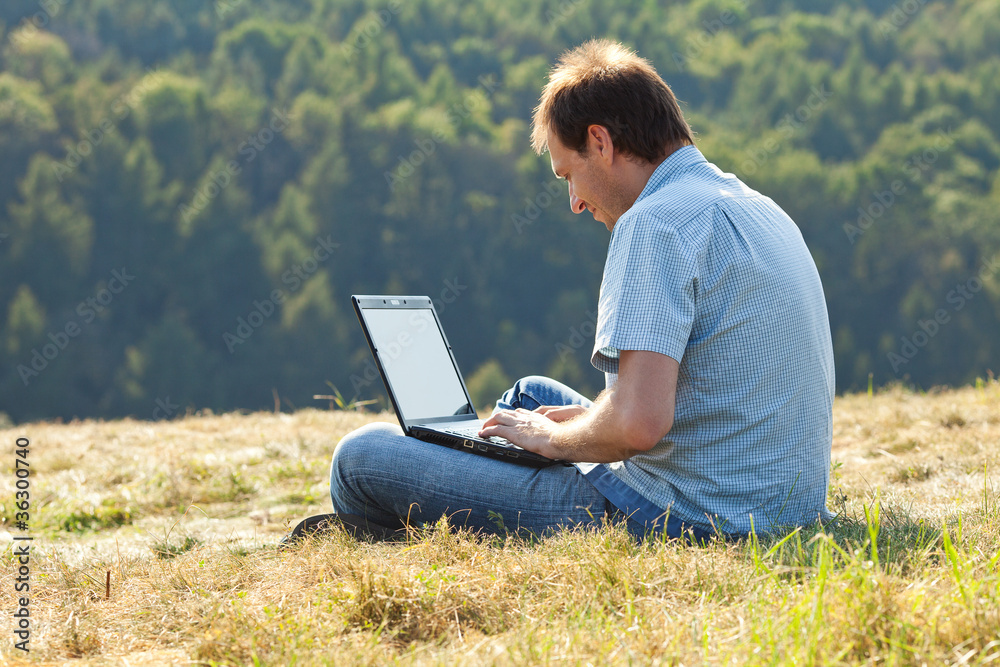 young man using laptop sitting on the grass on the hillside young man using laptop sitting on the grass on the hillside