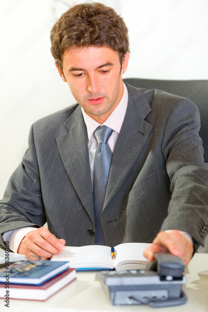 Sitting at office desk modern businessman pick up phone Sitting at office desk modern businessman pick up phone