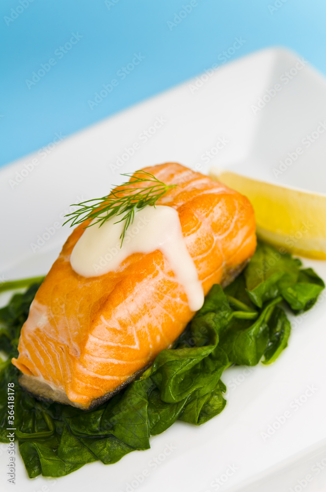 Salmon steak on spinach, decorated with lemon, dill and sauce Salmon steak on spinach, decorated with lemon, dill and sauce