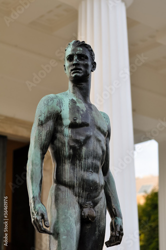 bronze statue of a athletic male body in front of a greek temple