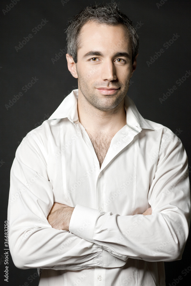 Handsome man posing in white shirt on dark background.