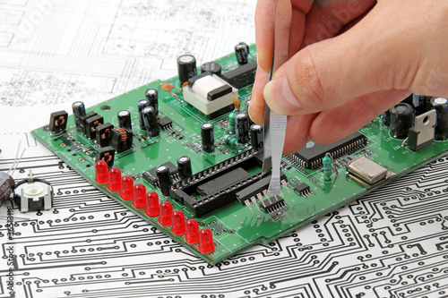 A hand hand with tweezers holding a electronic circuit board on