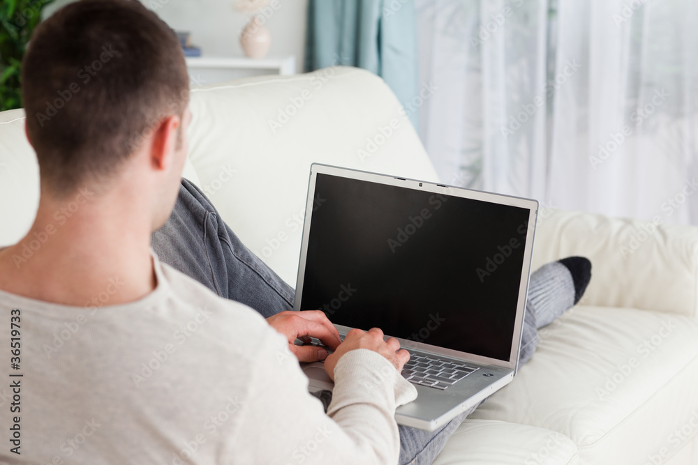 Man lying on his couch to use a laptop