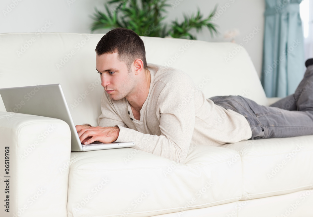 Young man lying on a sofa using a laptop Young man lying on a sofa using a laptop