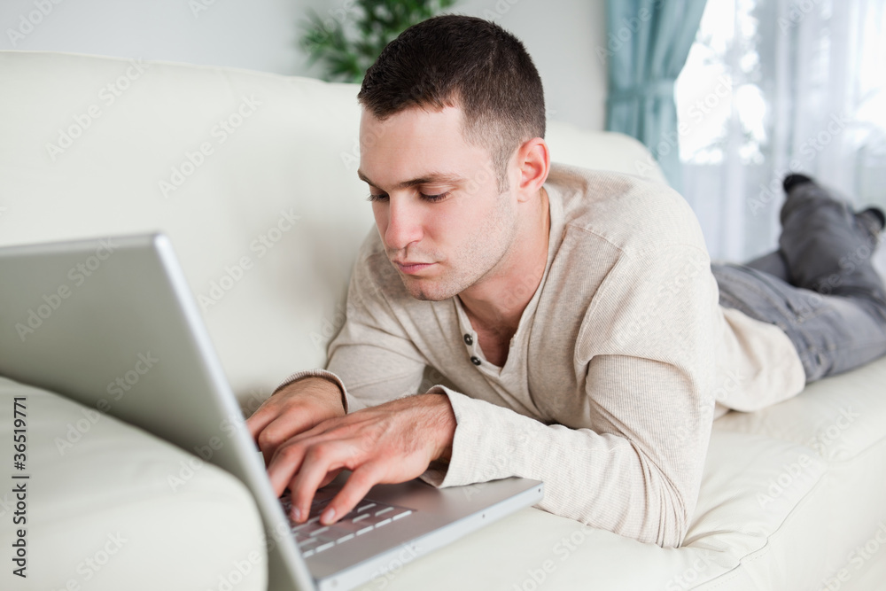 Focused man lying on a sofa using a laptop