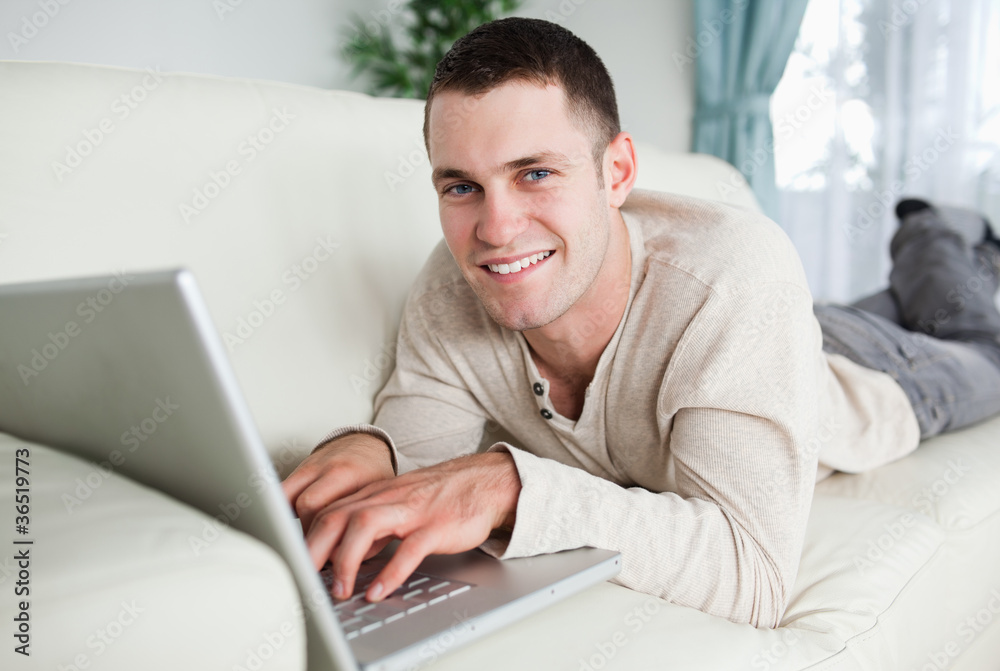 Smiling man lying on a couch with a laptop Smiling man lying on a couch with a laptop