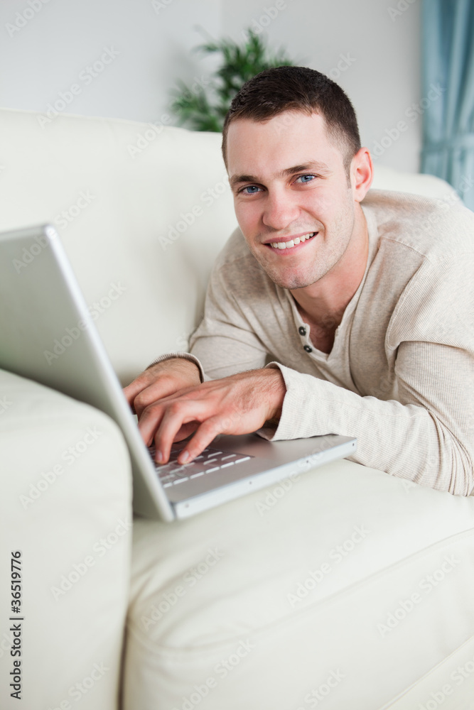 Portrait of a smiling man lying on a couch with a laptop Portrait of a smiling man lying on a couch with a laptop